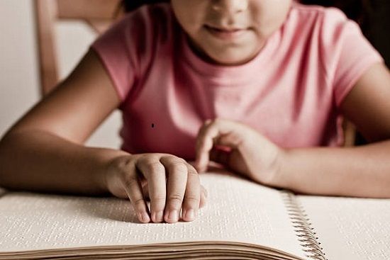 Mani di una bimba che leggono un libro in braille