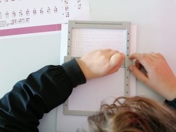 photo of a student writing with an awl on a braille tablet