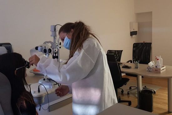 Una dottoressa misura la vista a una paziente sdraiata sulla poltrona delle visite nel centro officina dei sensi