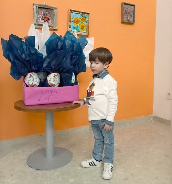 bambino di nome Alessandro in piedi vicino ad un cesto pieno di uova al cioccolato